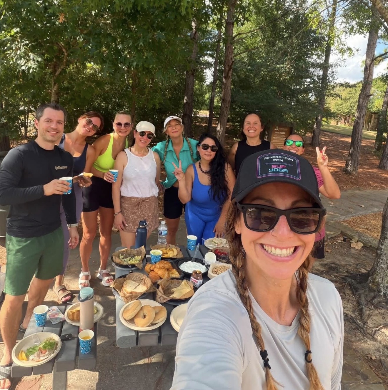 The Paddle Crew smiling together at a picnic after a morning paddle, wearing a Generation Zen SUP Yoga cap