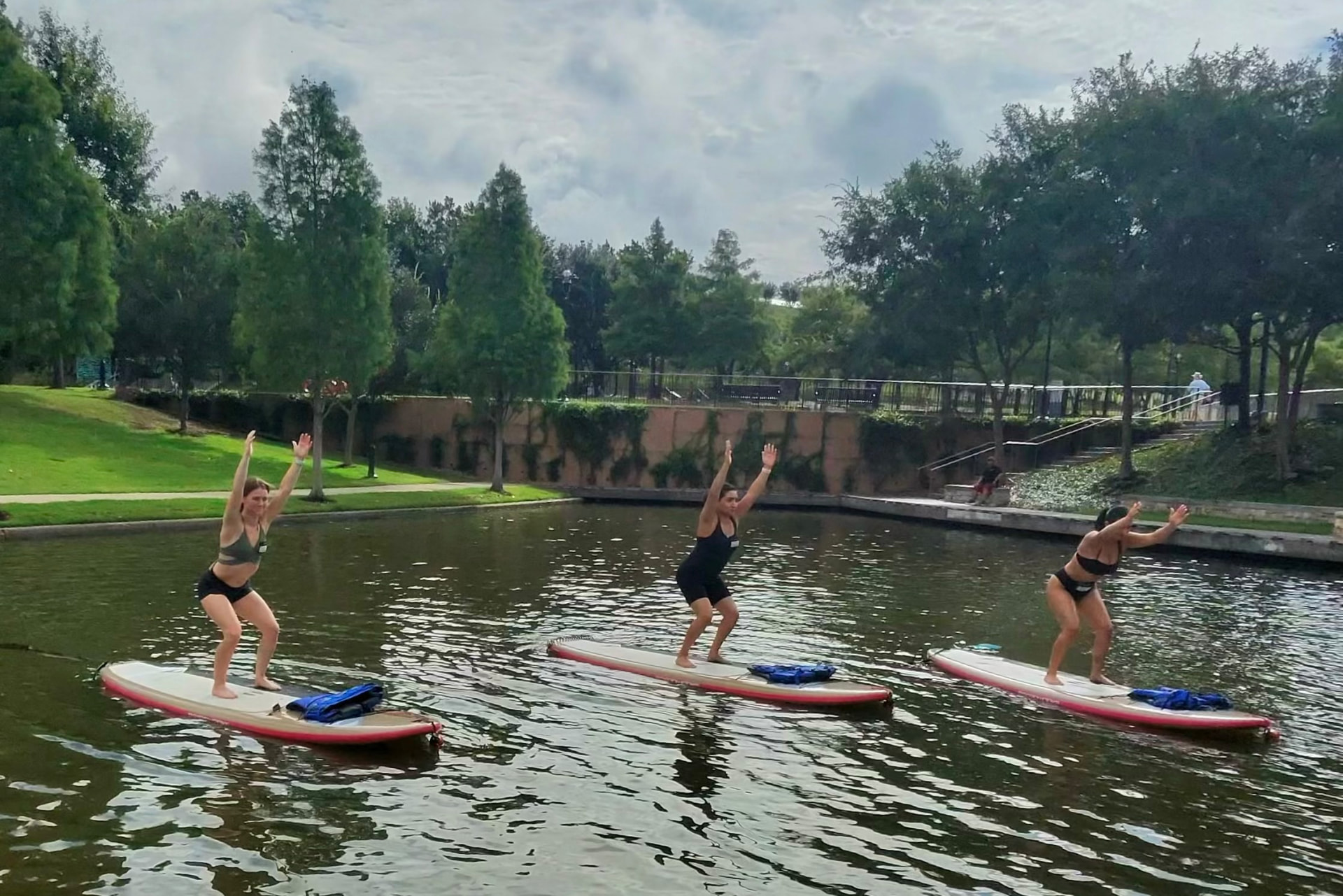 Three paddlers raising their arms in chair pose on paddleboards on The Woodlands Waterway