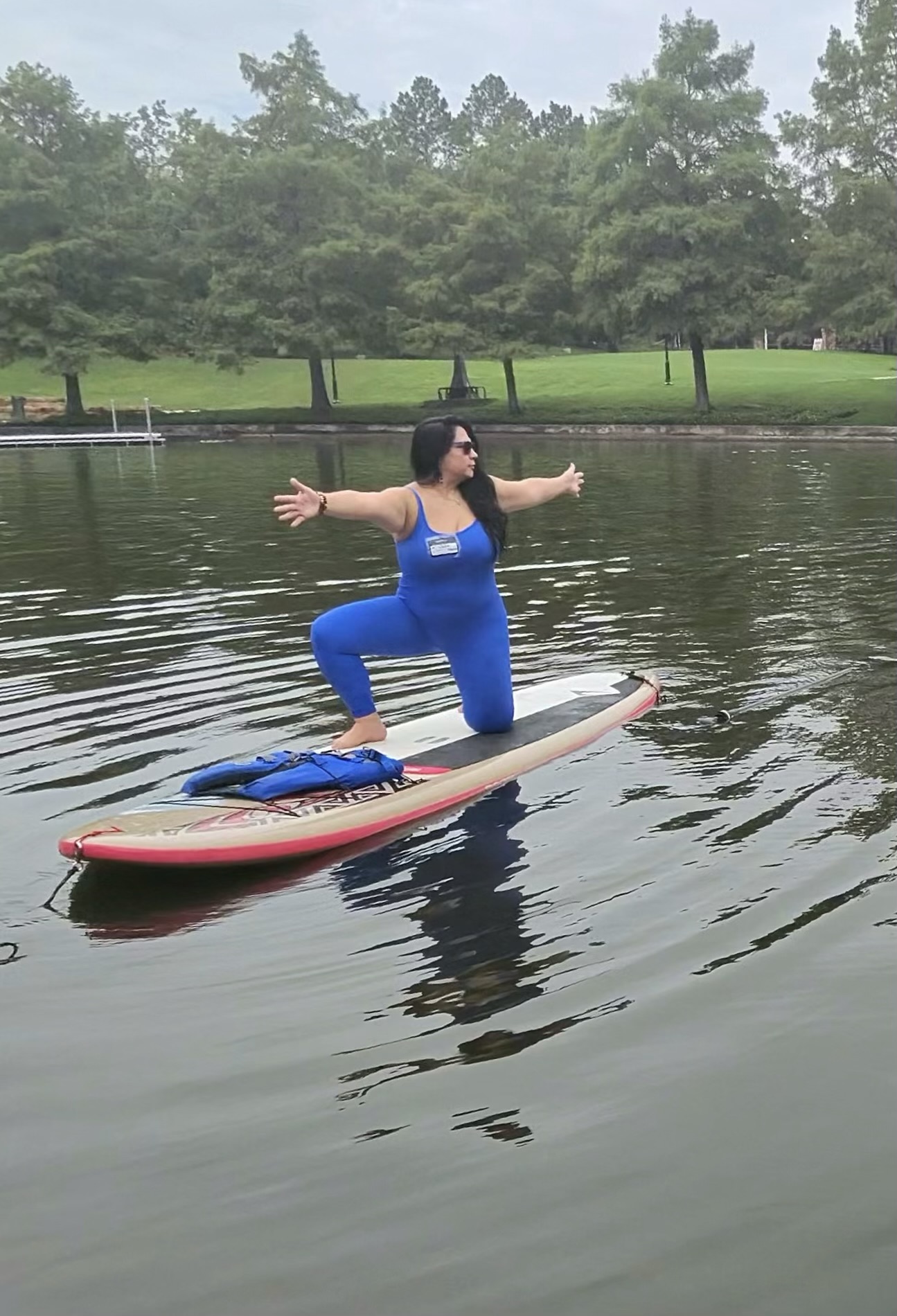 A woman in a low lunge with arms extended on a paddleboard on a tree-lined lake