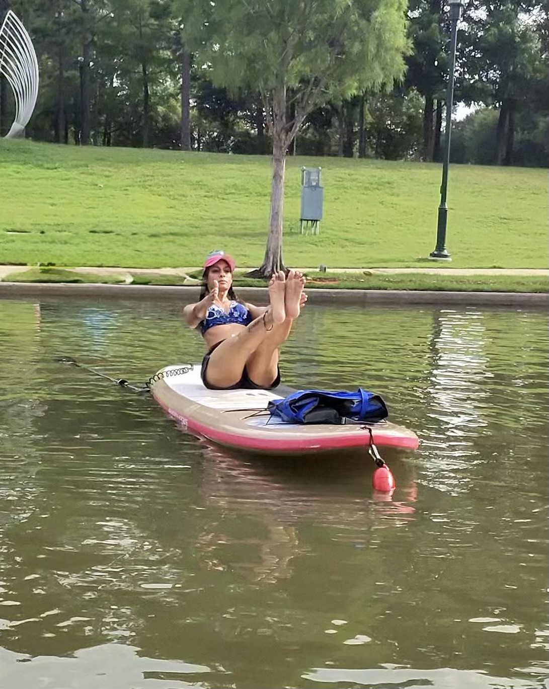Instructor balancing in boat pose on a paddleboard on a calm lake at The Woodlands Boathouse