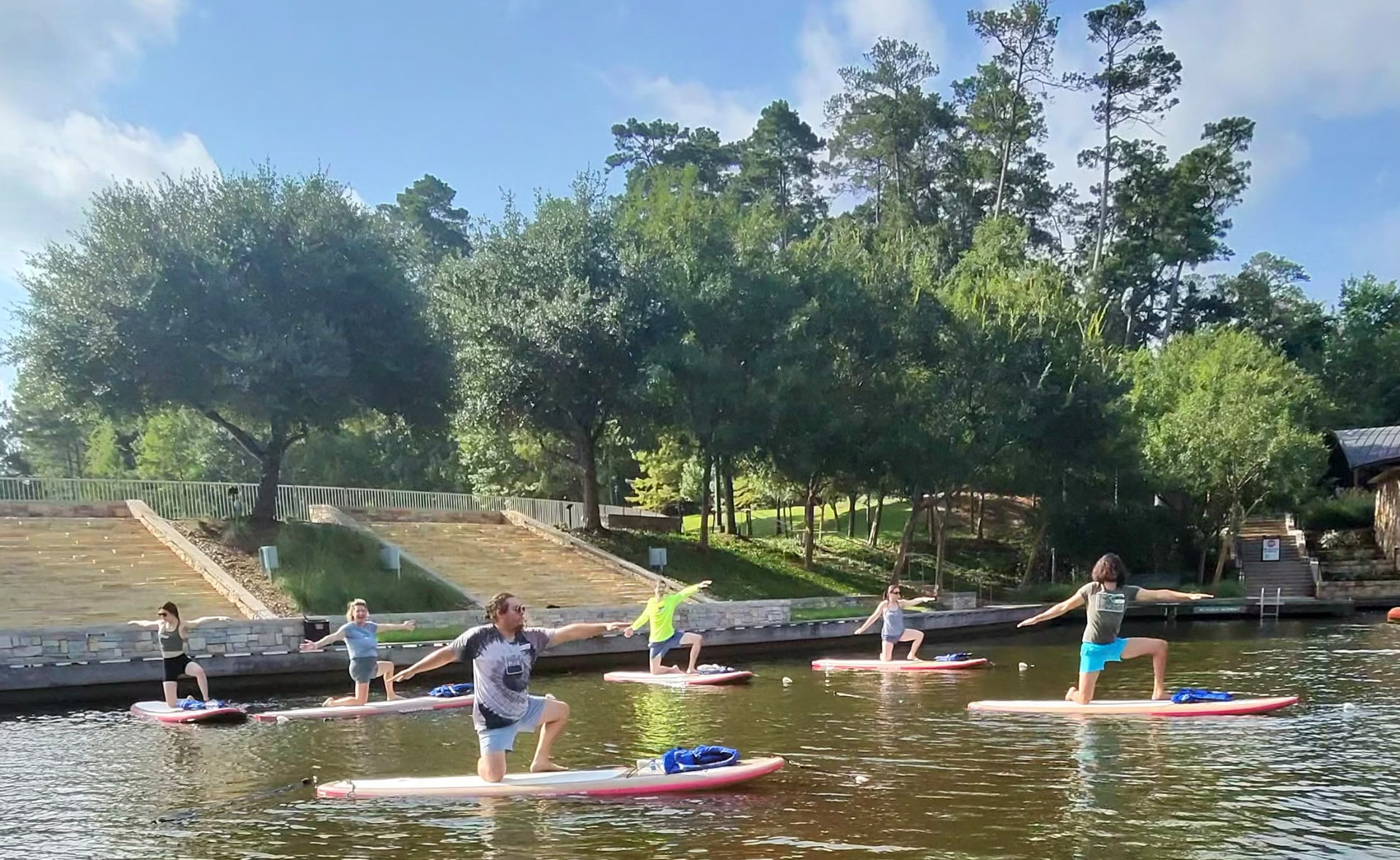 A group class holding warrior pose on paddleboards along The Woodlands Waterway